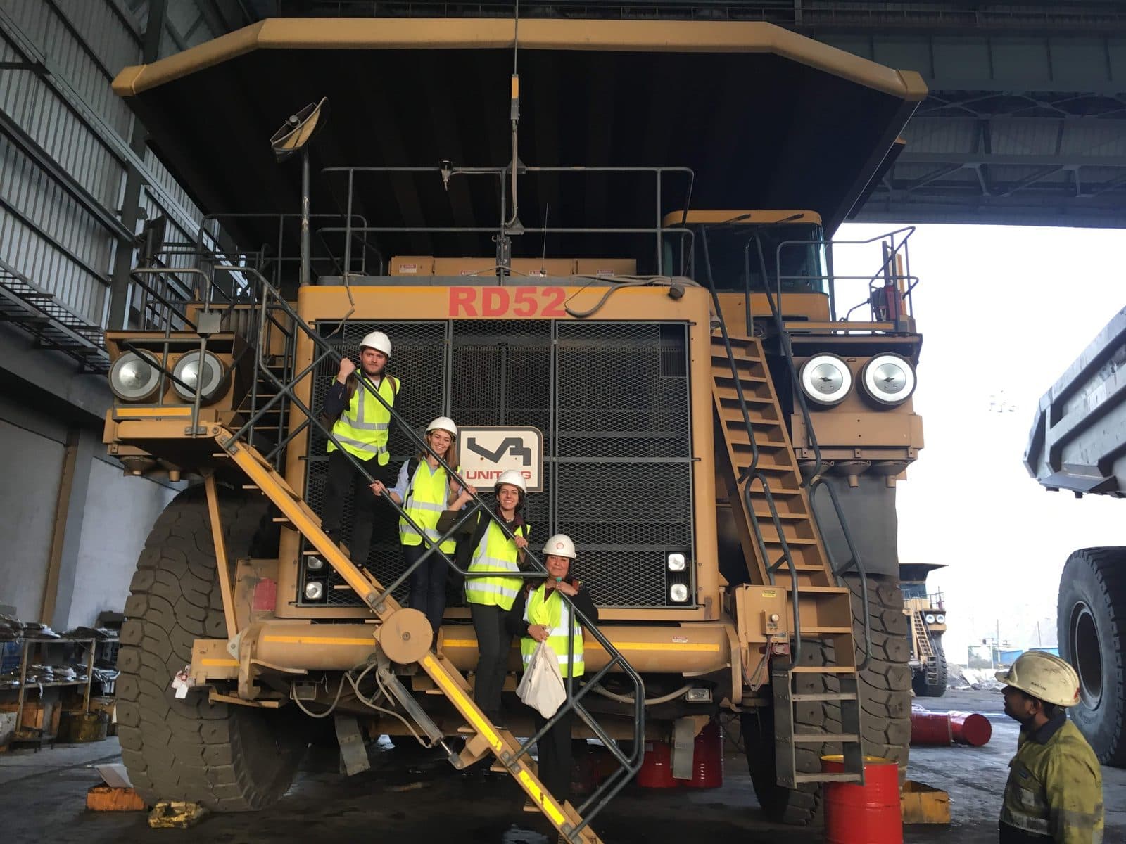 Lucy and three colleagues in hard hats and hi-vis vests on the steps of a large mining haul truck