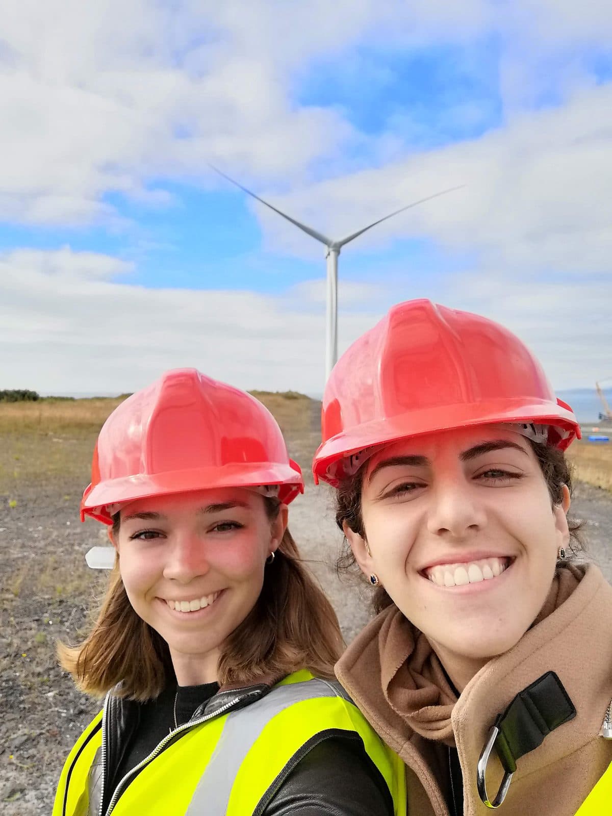 Lucy and a colleague in red hard hats in front of a wind turbine